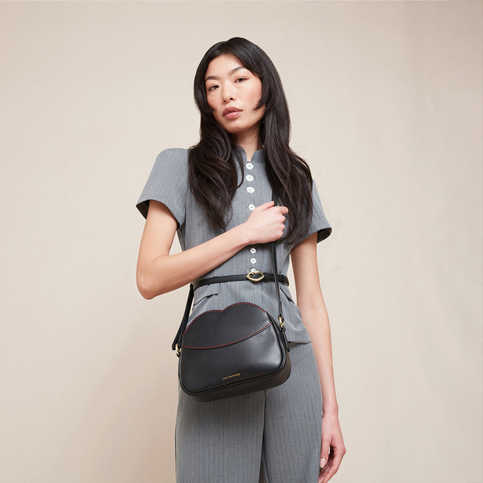 Women wearing a grey suit and a black leather crossbody bag with red stitched details.