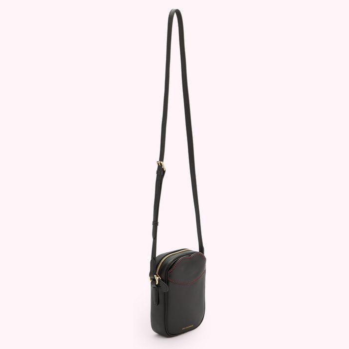 A image of a black leather crossbody bag with contrasting red lip shaped stitching on the front pocket with the strap help up.
