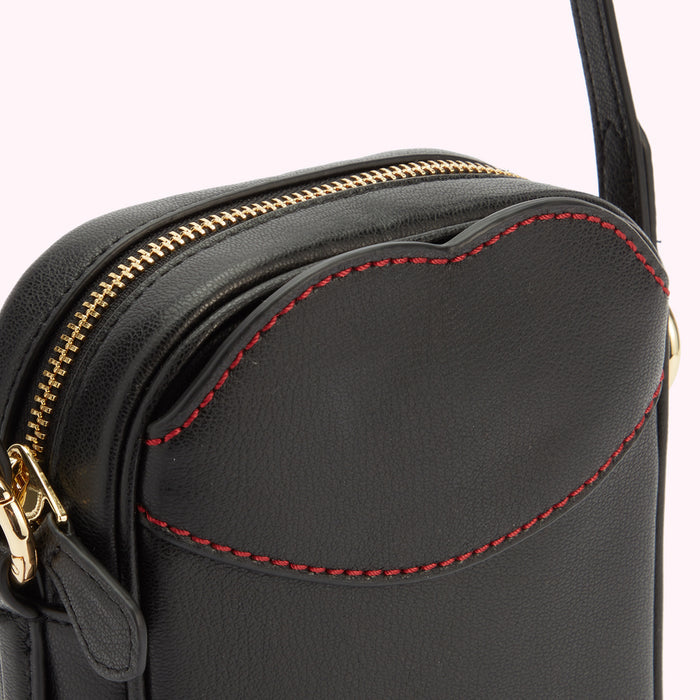 A close-up detail of a black leather bag with a gold metal zip and zip pull and contrasting red lip shaped stitching on the front pocket.