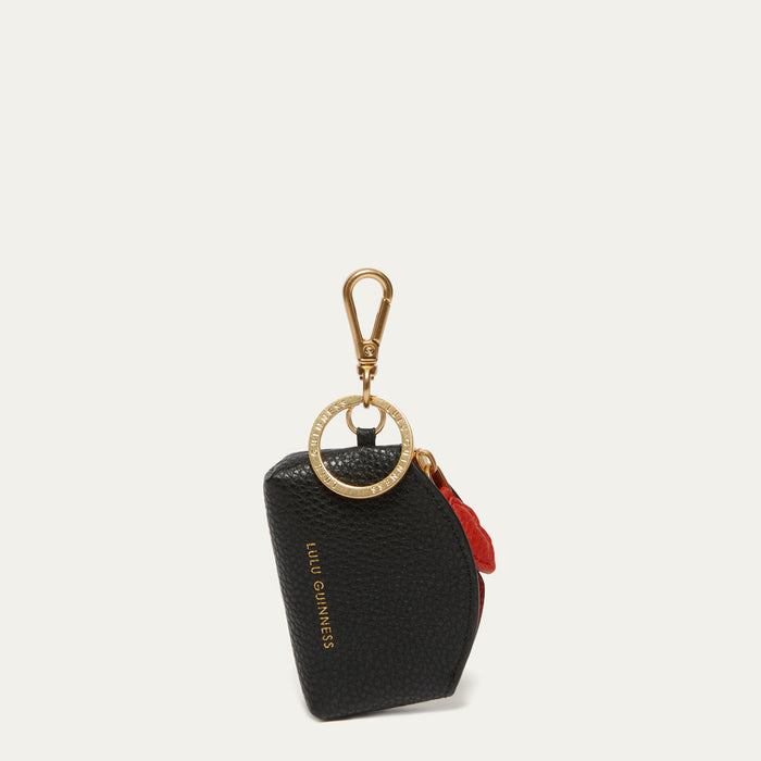 A black pebbled leather key pouch with gold-tone hardware, featuring a gold-tone ring clasp, a red leather accent tab, and gold 'LULU GUINNESS' branding on the front, set against a light off-white background.