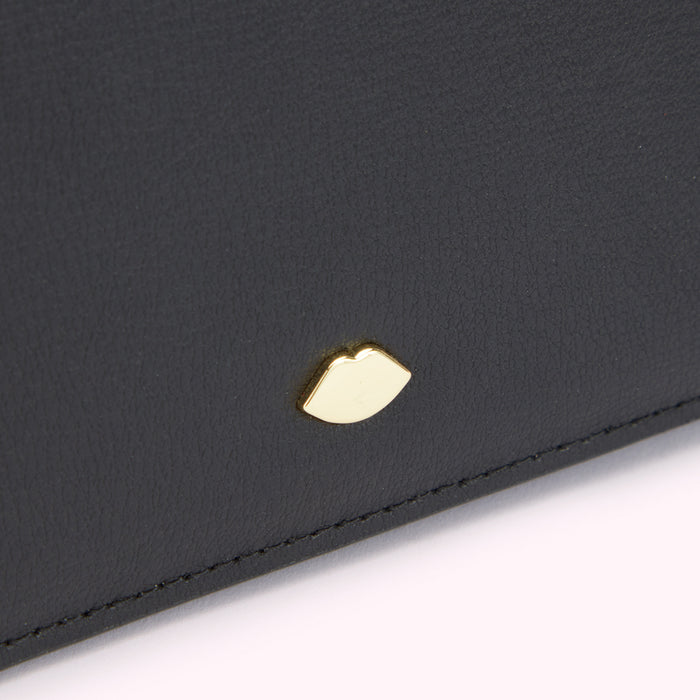 Close up image of a gold lip shaped pin on a black leather bag.
