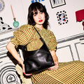 Model with dark hair wearing a yellow striped dress and holding a black leather shoulder bag.