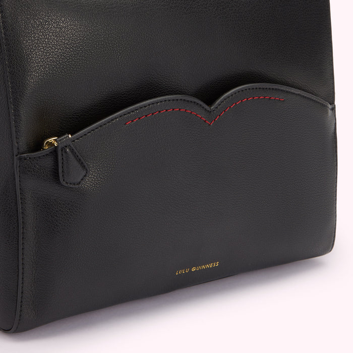 Detail close up image of black leather shoulder bag front pocket with contrasting red stitch detailing.