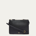 Black leather crossbody bag with gold lip pin on a light gray background