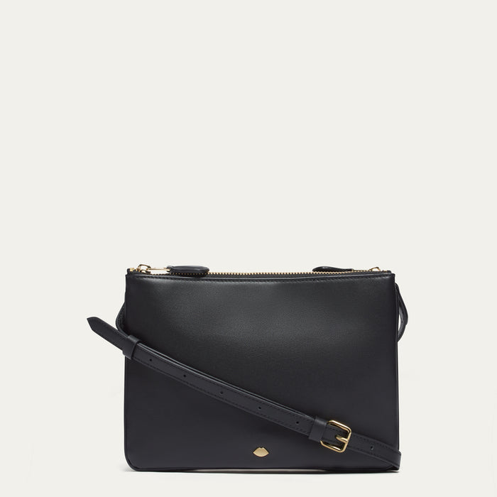 Black leather crossbody bag with gold lip pin on a light gray background
