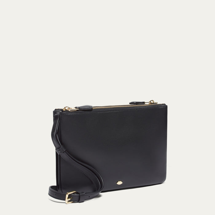 Black crossbody bag with a gold lip pin on a light beige background