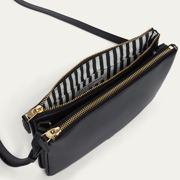 Black handbag with gold zipper open to show a striped lining on a white background