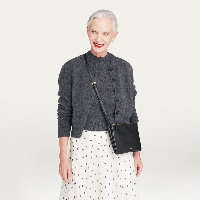 Woman wearing a gray cardigan and white skirt with a black handbag on a light gray background