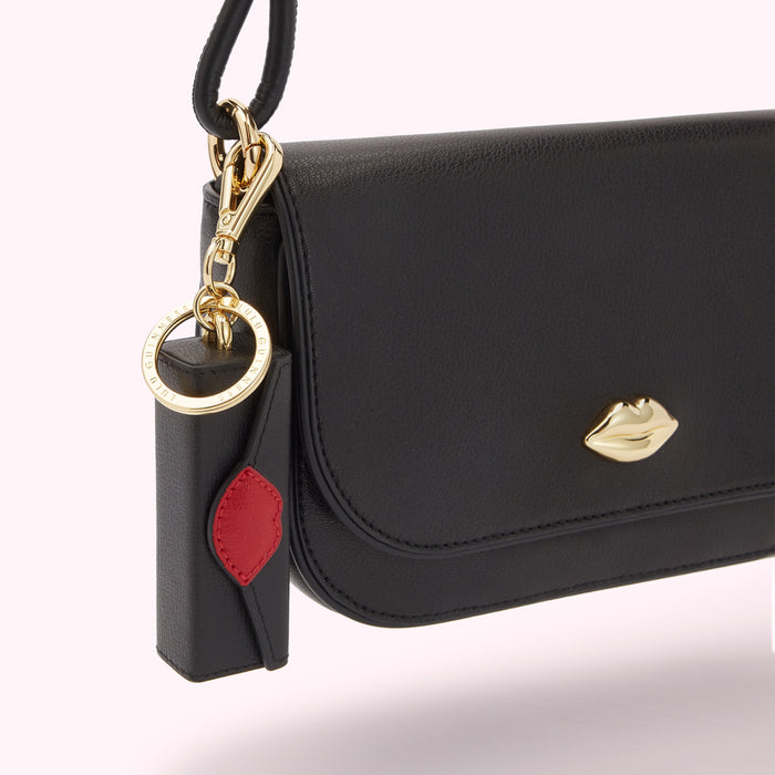 Close-up of a black leather crossbody bag with a gold lip-shaped detail and a matching lipstick-shaped keychain.