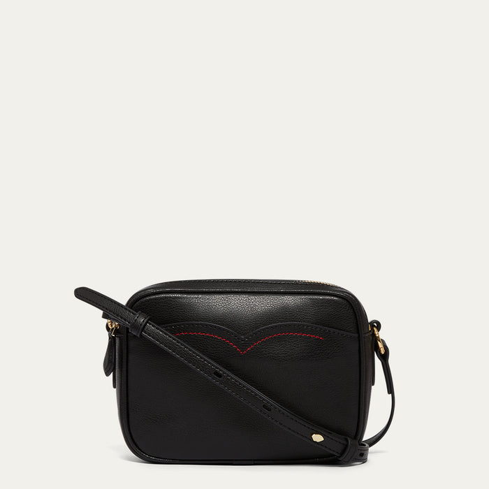 Black leather crossbody bag with red stitching on a light grey background