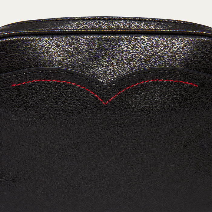 Close-up of black leather handbag with red stitching on a light grey background