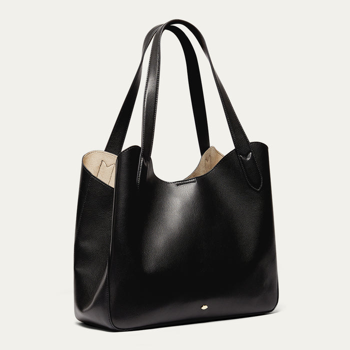 Black leather tote bag with a beige interior on a light grey background
