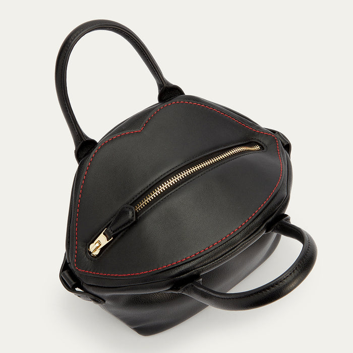A above image of the top of a black leather handbag showing the gold zip fastening and lip shaped contrasting red stitching.