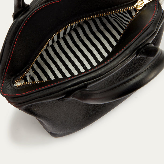 A close-up image of a black leather handbag open revealing the white and black striped lining and contrasting red stitching across the top.