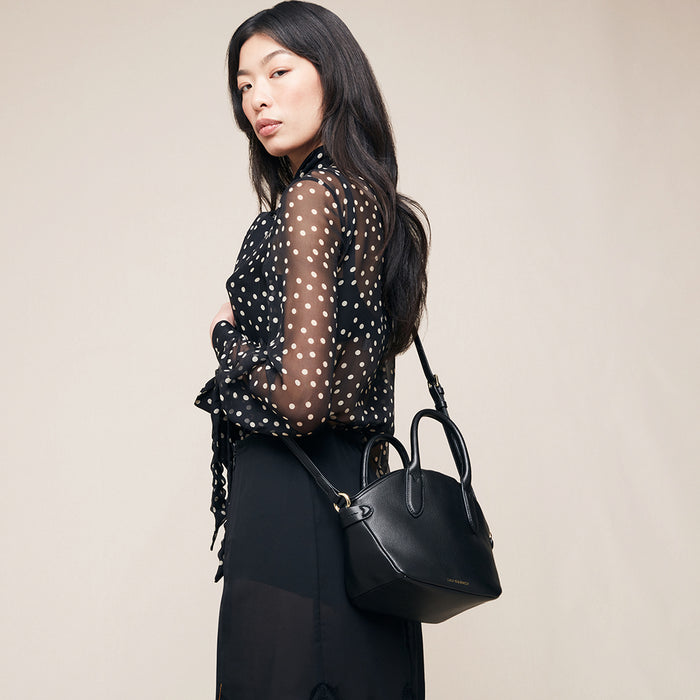 Woman holding a black handbag against a beige background