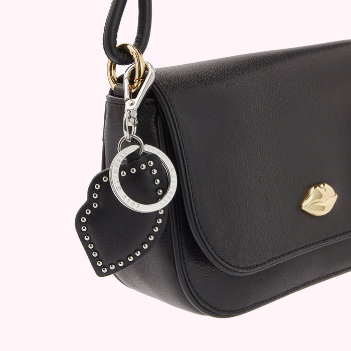 Close-up of a black Lulu Guinness handbag with a lip-shaped charm and a studded heart-shaped keychain.
