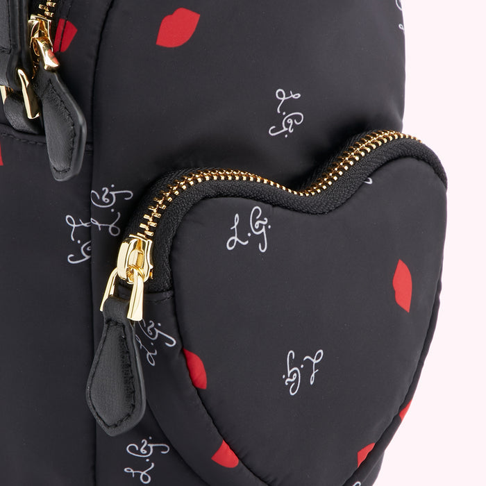 Close-up of a black heart-shaped bag with a gold zipper, featuring a lip print and a logo.