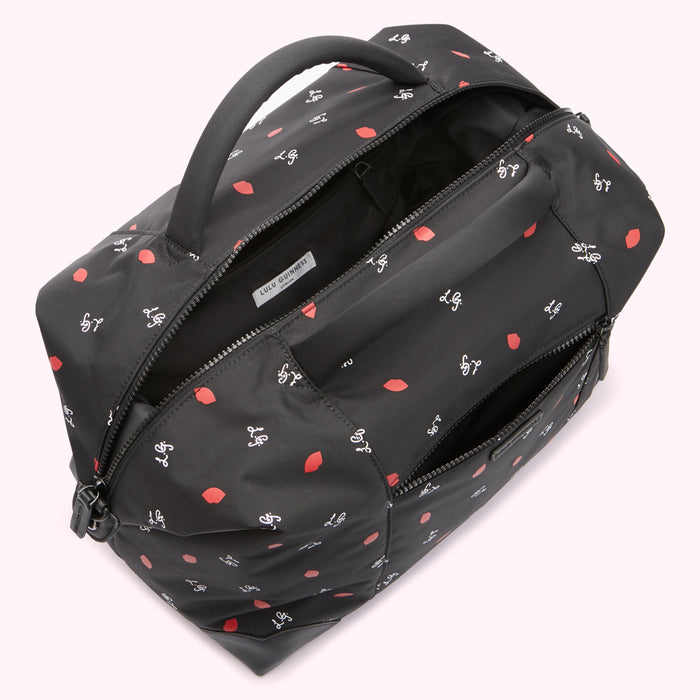 Overhead view of a black Lulu Guinness bag with a red lip print, open to show the interior.