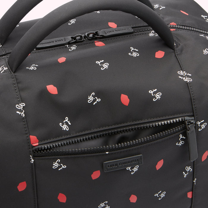 Close-up of a black Lulu Guinness travel bag with a red lips and white logo print.