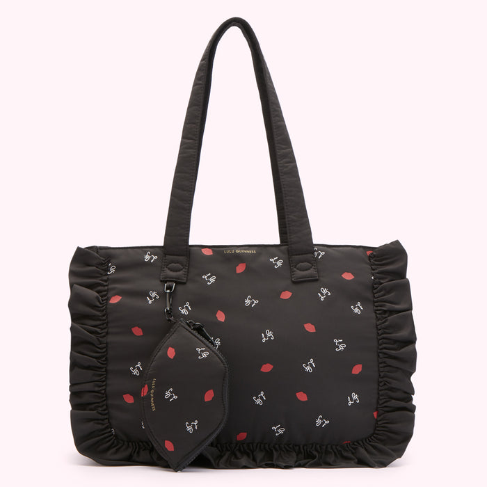 Black tote bag with ruffled edges and a repeating pattern of red lips and the Lulu Guinness logo. A smaller matching zippered pouch is attached to the bag.