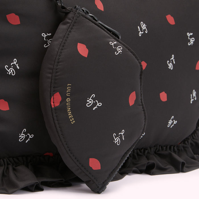Close-up of a black Lulu Guinness bag and matching pouch featuring a red lips and cursive logo print.