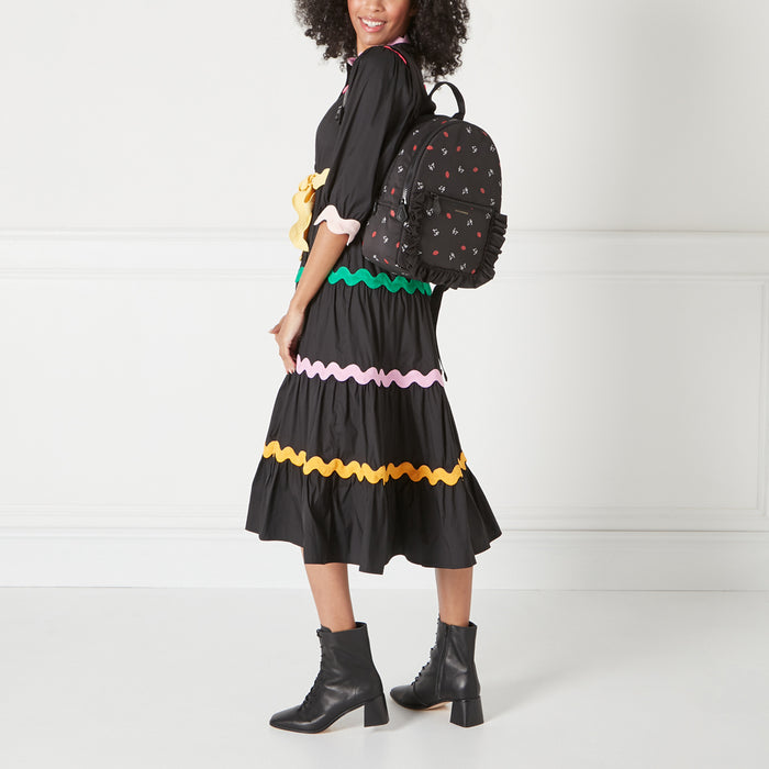 A woman in a black dress with colourful trim is wearing a black backpack with a red lip and other small prints on it.