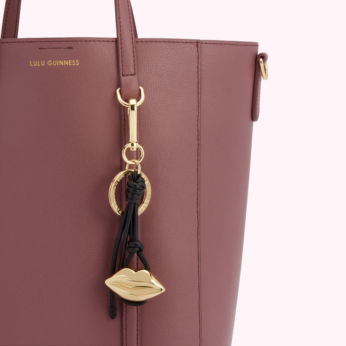 Close-up of a dusty rose Lulu Guinness tote bag with a gold lip-shaped keychain.