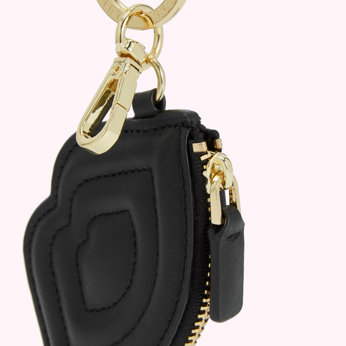 Close-up of a black leather keychain with gold hardware. The keychain is shaped like a heart and has a zipper closure.