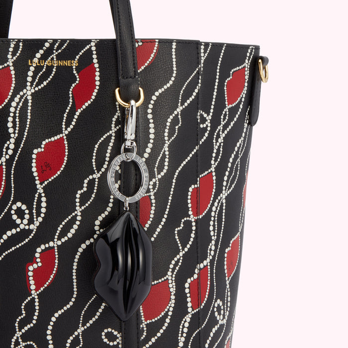 Close-up of a Lulu Guinness black tote bag with a red lip print and pearl detailing, featuring a lip-shaped keychain charm.