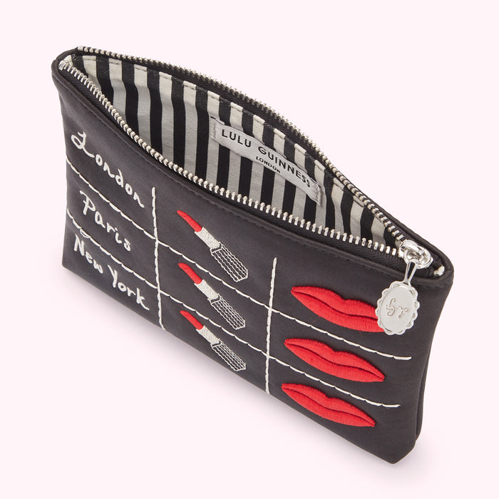 Black Lulu Guinness makeup bag with embroidered lips and lipsticks, and the words "London," "Paris," and "New York" stitched on the front.