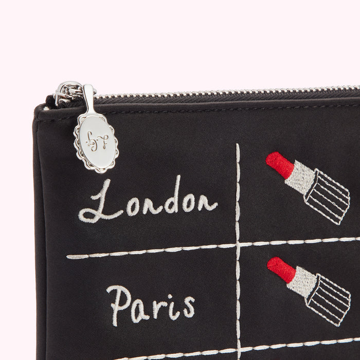Black makeup bag with embroidered lipstick and city names; London and Paris.