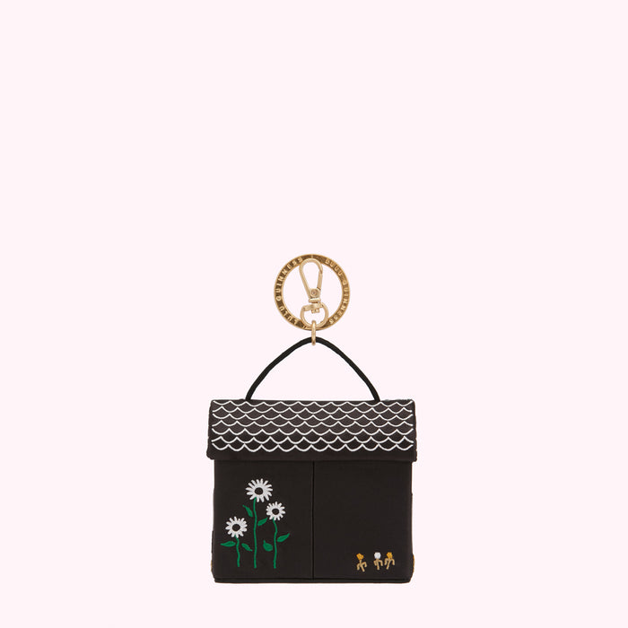 Black and white house-shaped keychain with gold ring, featuring embroidered flowers and small figures.