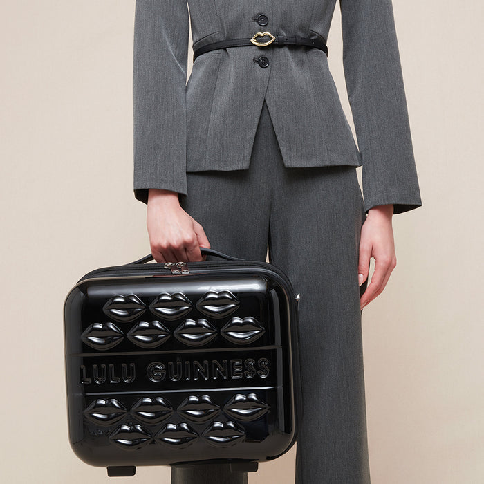 Women in a grey suit holding a black hard shell vanity case with lip detail and Lulu Guinness branding.