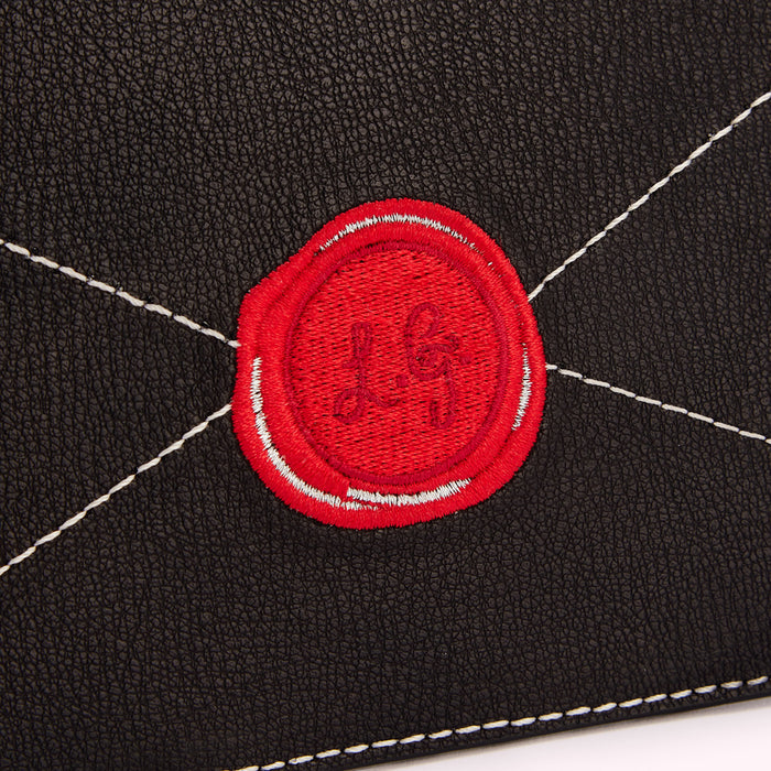 Close-up of a black leather surface with a red embroidered wax seal bearing the initials "LG".