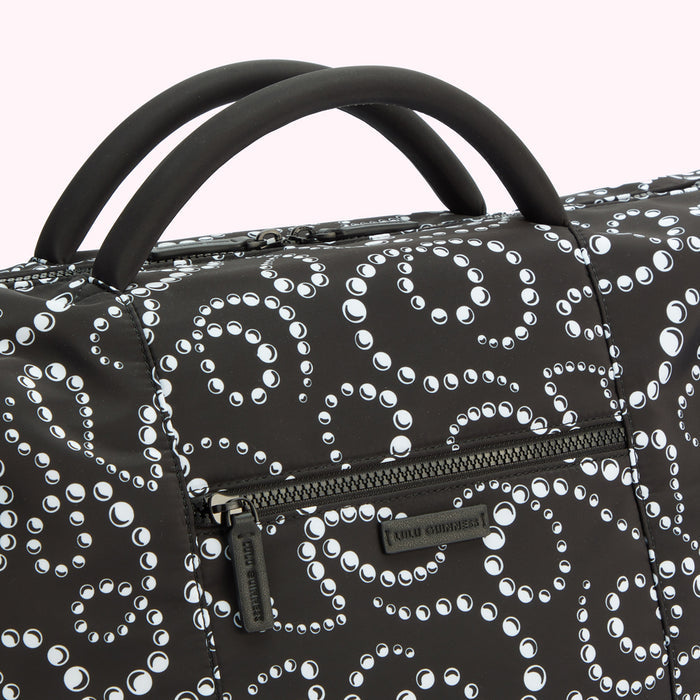Close-up of a black Lulu Guinness handbag with a white pearl pattern; the bag has two short top handles.