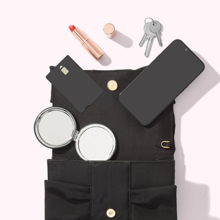 A black handbag open to reveal its contents: a smartphone, credit card, lipstick, compact mirror, and keys. The background is white.