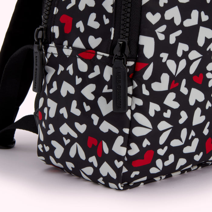 Close-up of a Lulu Guinness black backpack with a white and red heart pattern.