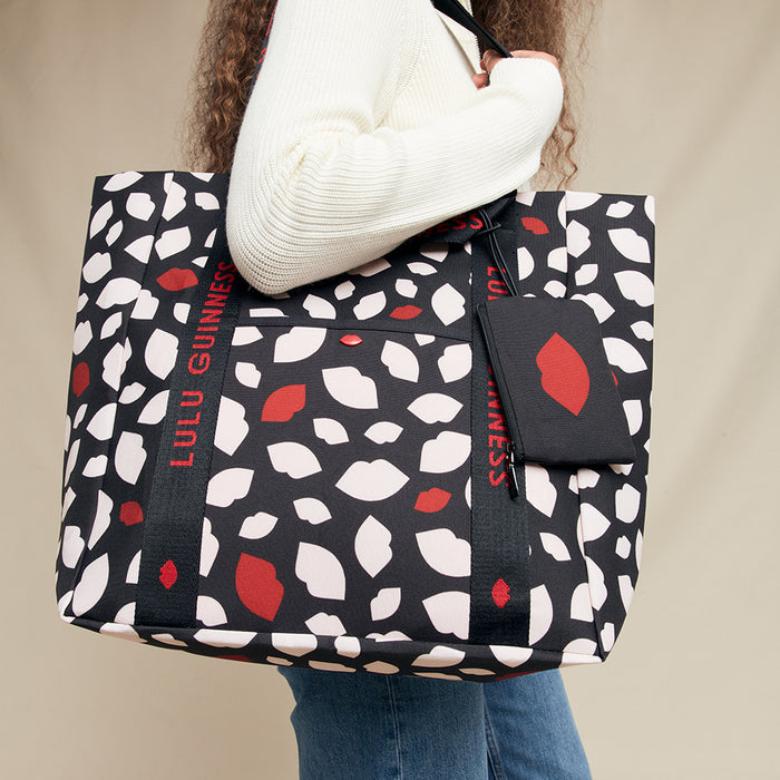 Person holding a black tote bag with red and white pattern, featuring 'Lulu Guinness' branding.