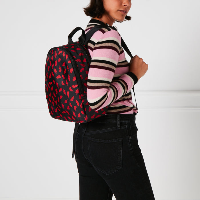 Woman wearing black jeans and pink and brown striped sweater with a black backpack covered in a red lip print.
