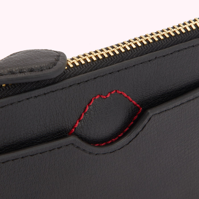Close-up of a black leather wallet with a red stitched lip detail and gold zipper.