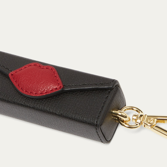 Black leather key charm with a red lip patch and gold keychain on a light grey background