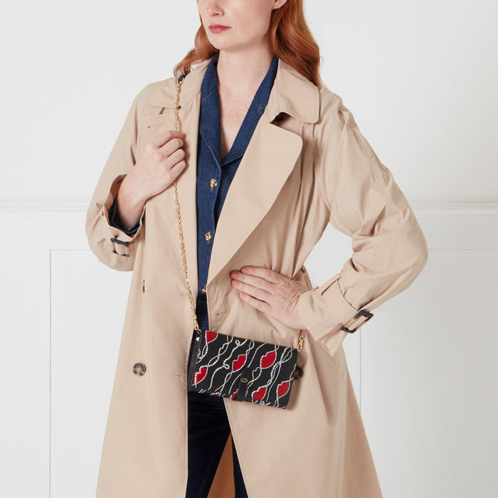 Woman wearing a beige trench coat and a black crossbody bag with red lips pattern.