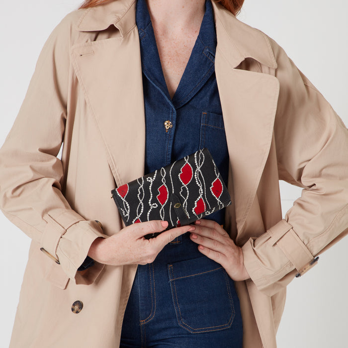 Woman holding a black wallet with red lips and white pearls on a beige background.