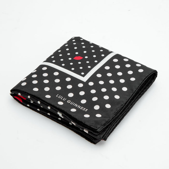 Black silk scarf with white polka dots and a red lip print; folded. The Lulu Guinness logo is visible.