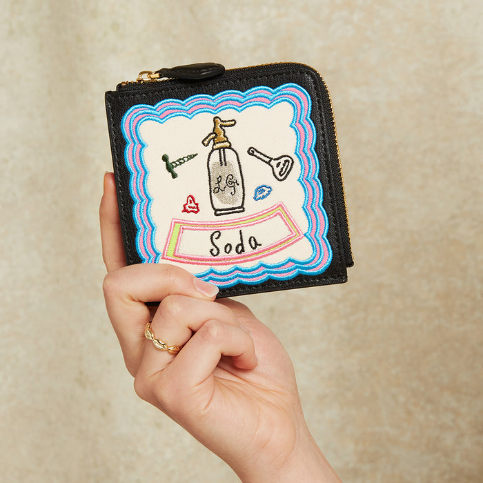 Hand holding a small black wallet with colourful design on a beige background