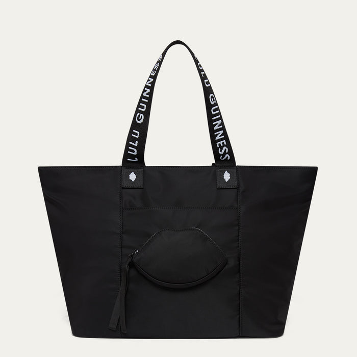 Black tote bag with Lulu Guinness handles and a lip-shaped pocket on a light grey background