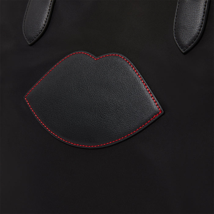 Black leather tote bag with red stitching shaped like lips on a black background