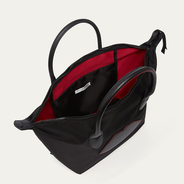 Black tote bag with lip detail open to reveal the inside pocket on a light gray background