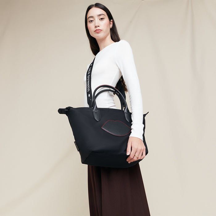 Woman holding a black nylon tote bag with detachable strap against a plain background
