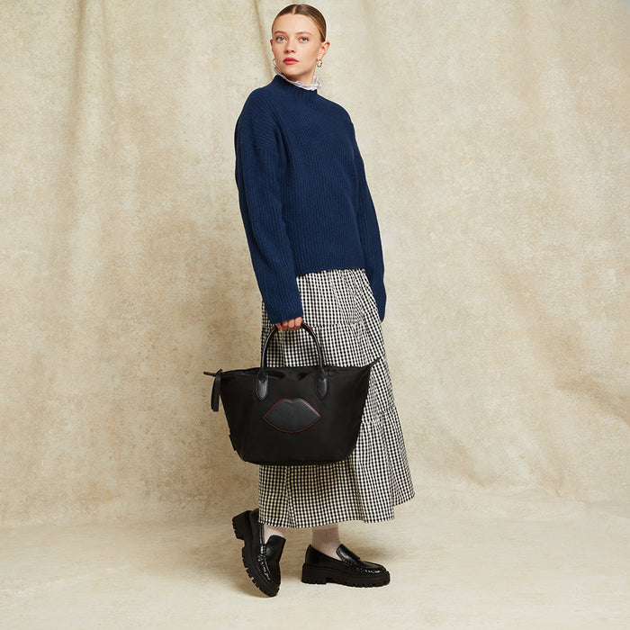 Woman holding a black handbag tote with lip detail against a beige background